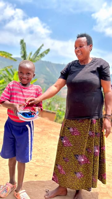A smiling boy receiving a gift from a woman at Green Hills, with hills behind them