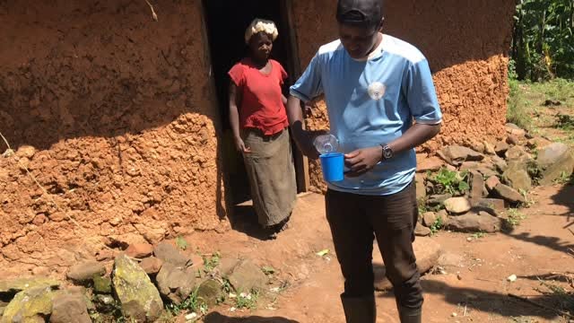 Thomas outside the mud house, with a woman standing in the doorway