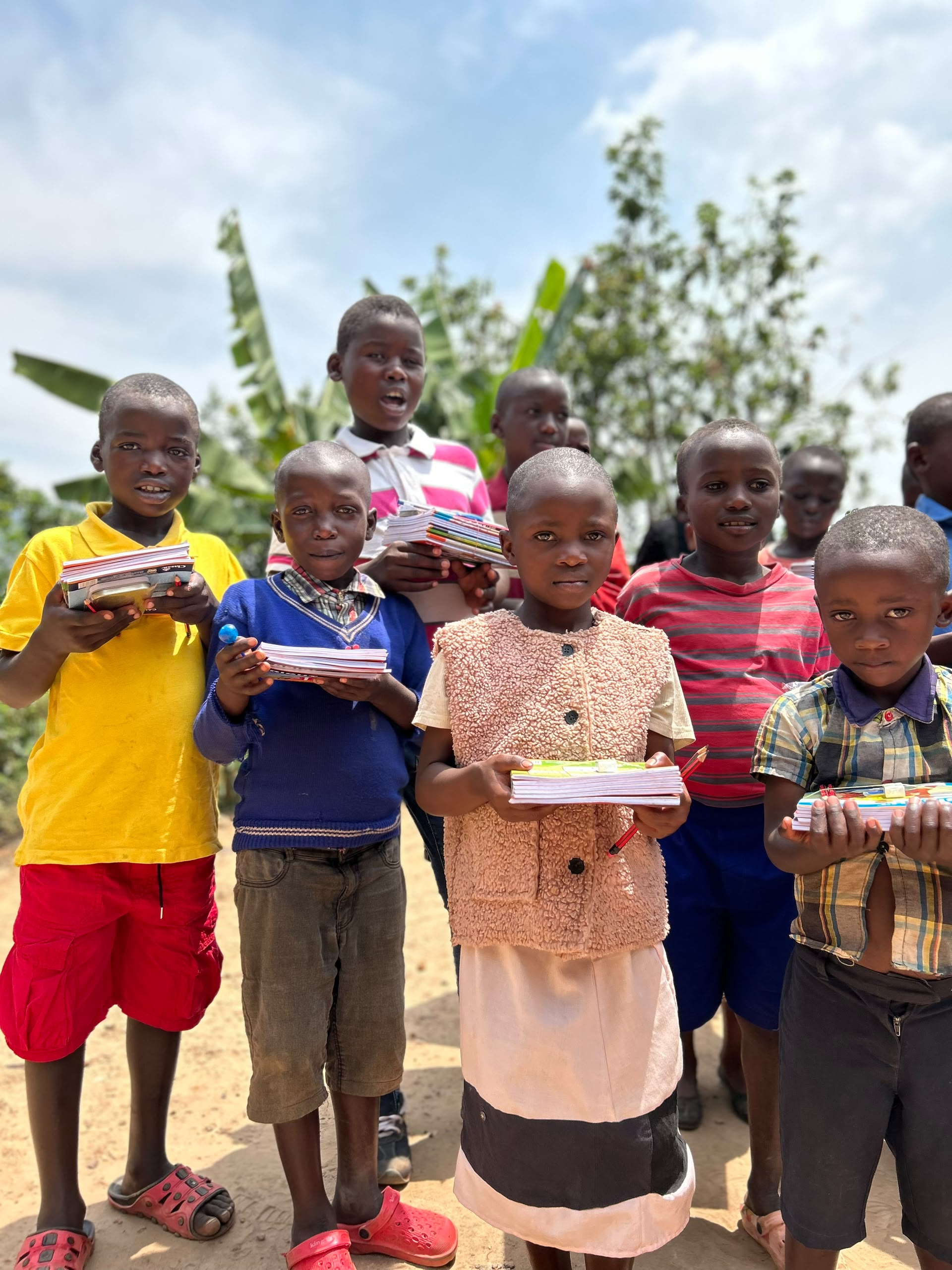 A group of children standing outside, each holding the exercise books and pencils they received