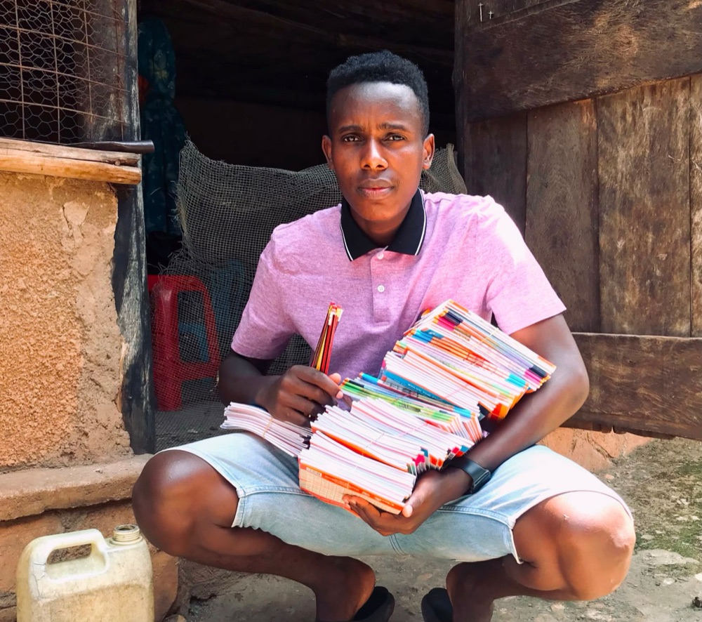 A young man crouching in a doorway with an armful of exercise books and pencils