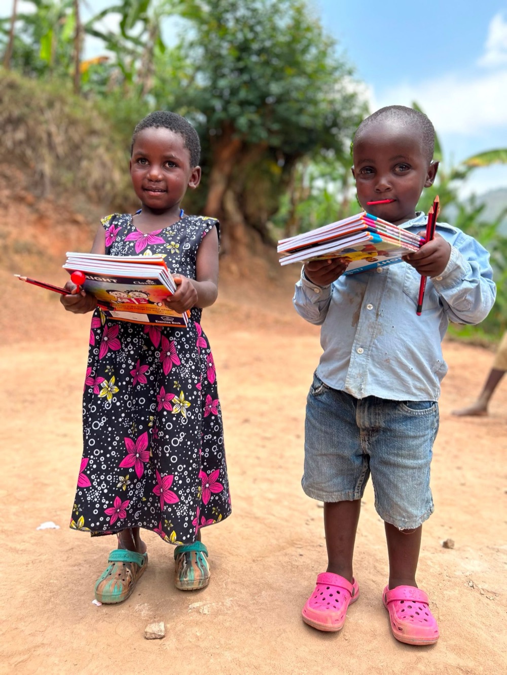 A little girl and a little boy each holding a stack of new exercise books and pencils
