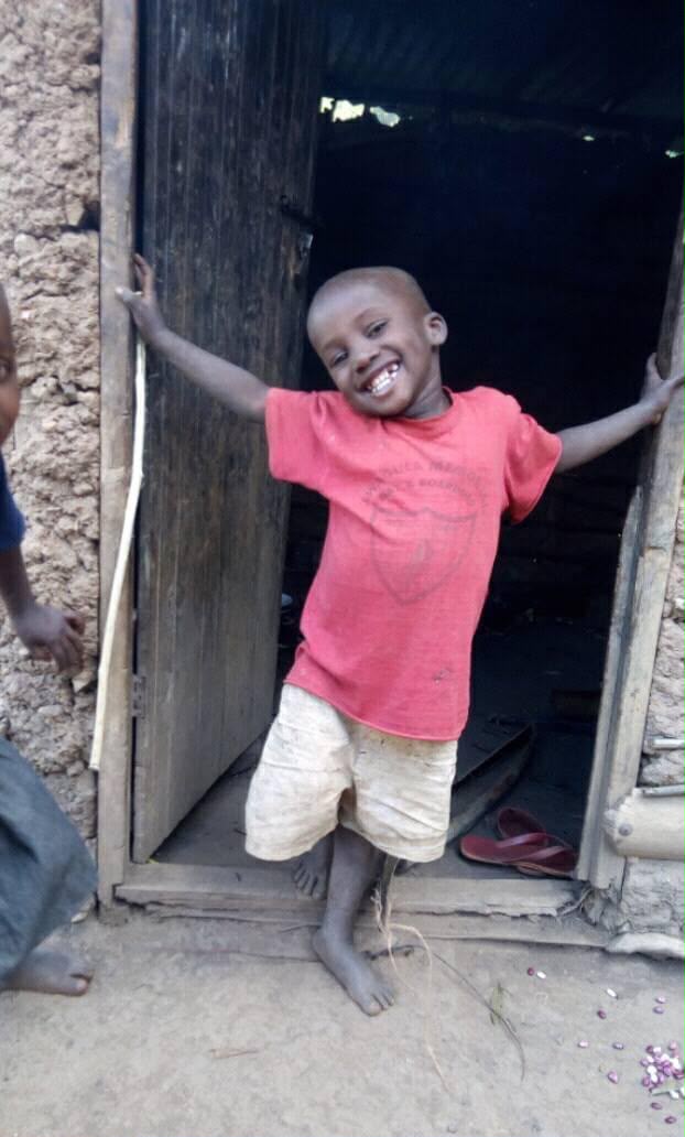 A smiling young boy in a red T-shirt standing in a doorway with his arms stretched wide