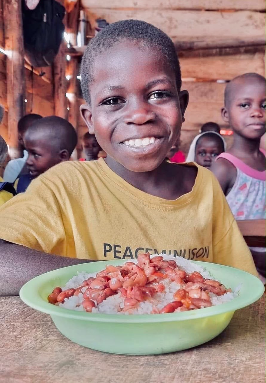 A boy in a yellow T-shirt grinning over a bowl of rice and beans
