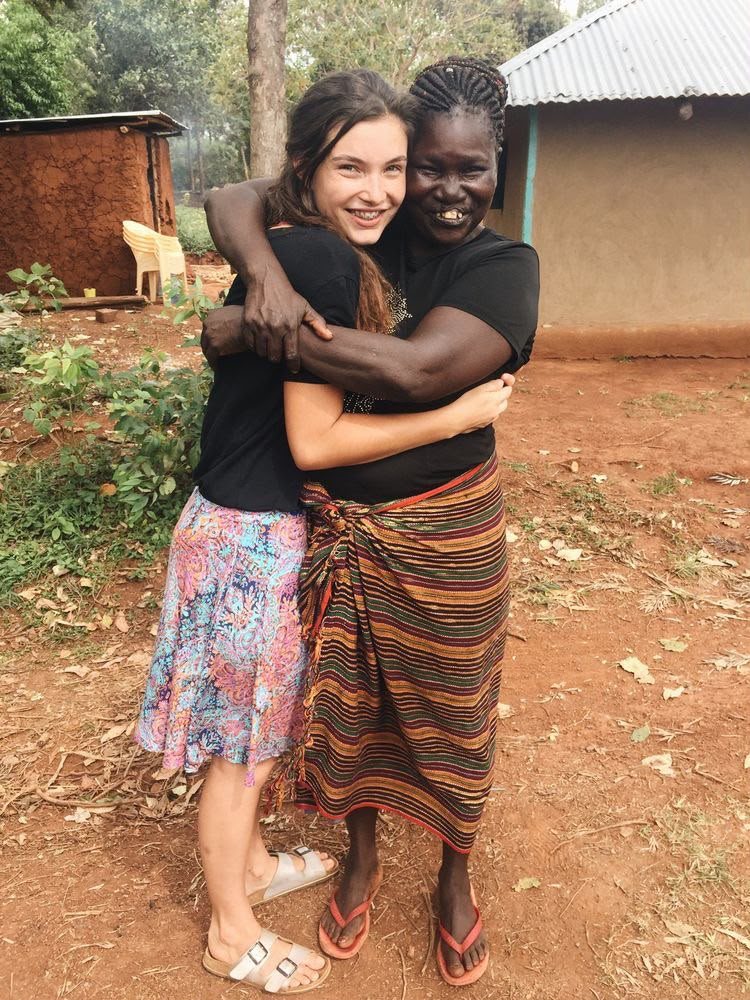 A volunteer and a woman from the community hugging outside a mud-brick house