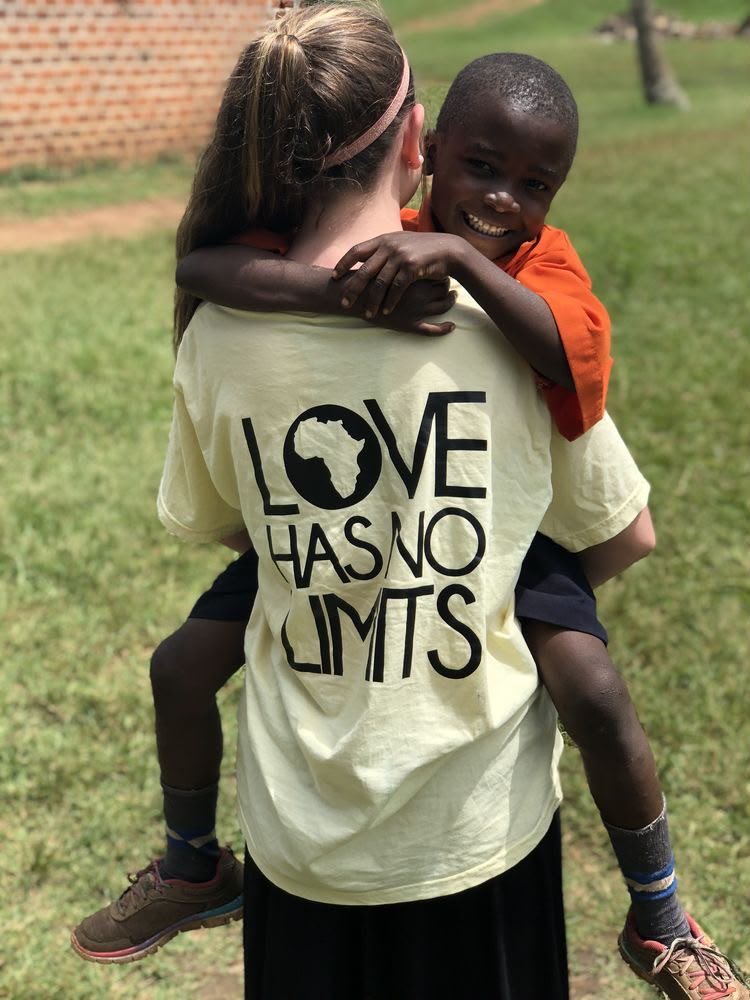 A boy on a volunteer's back, her T-shirt printed with Love has no limits and a map of Africa